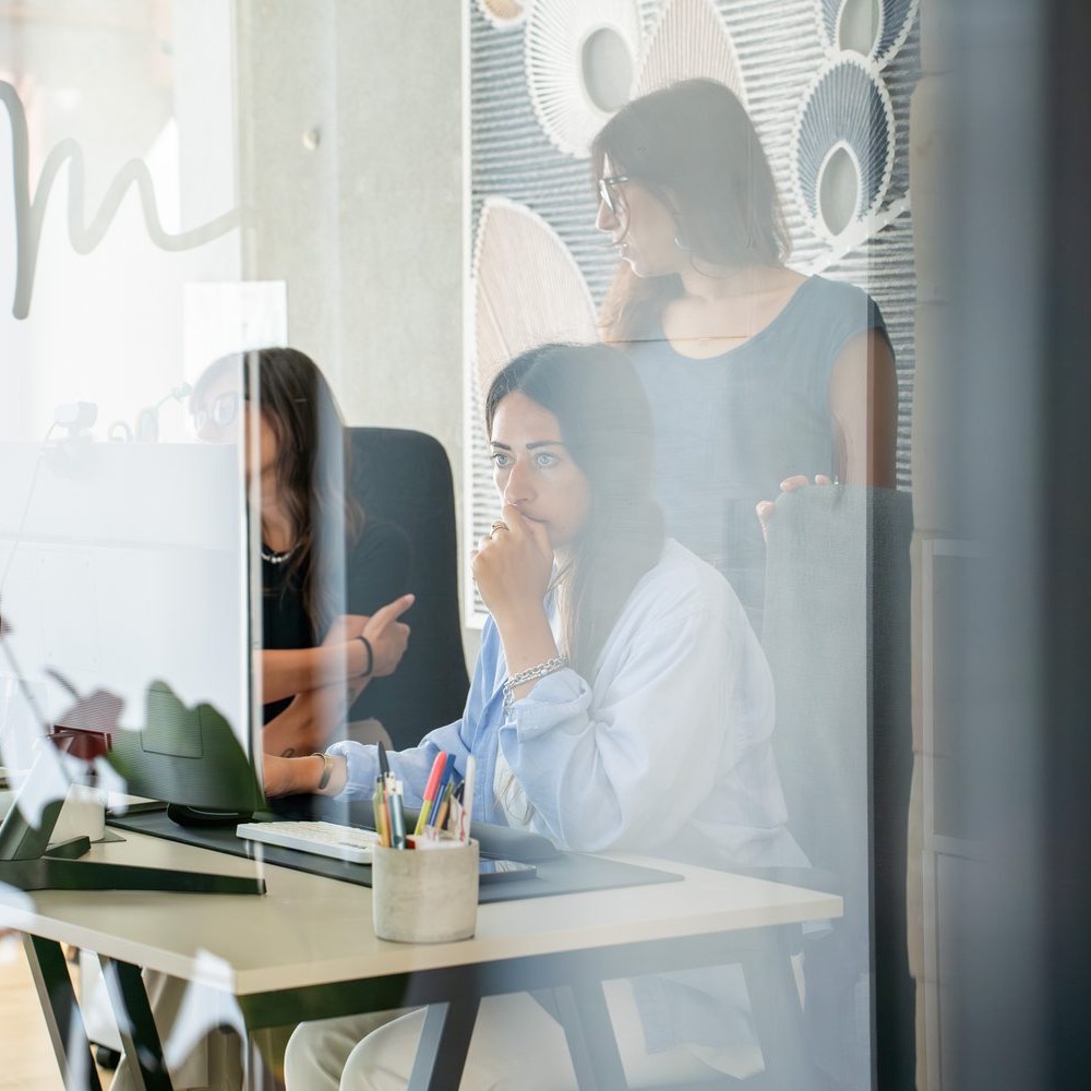 Due persone del team GOODCOM al lavoro, riprese attraverso una parete a vetri