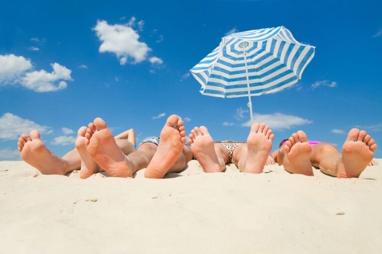 Piedi di un gruppo di persone distese sulla sabbia, per vacanze al mare all'insegna del turismo sostenibile