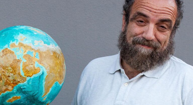 Giobbe Covatta accanto a un mappamondo, intervistato sul futuro del pianeta
