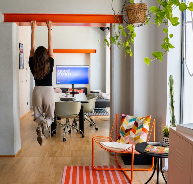 Alessandra del team appesa alla trave arancione dell'open space dello studio GOODCOM
