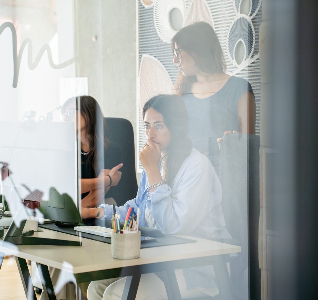 Due persone del team GOODCOM al lavoro, riprese attraverso una parete a vetri